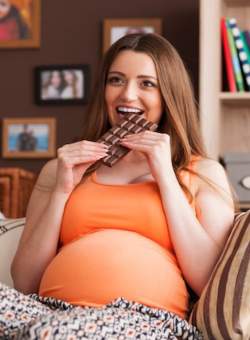 Gestante sentada no sofá comendo chocolate